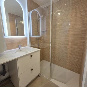 Vignette Salle de bains contemporaine associant des revêtements effet bois, une douche vitrée et un miroir rétroéclairé pour une ambiance